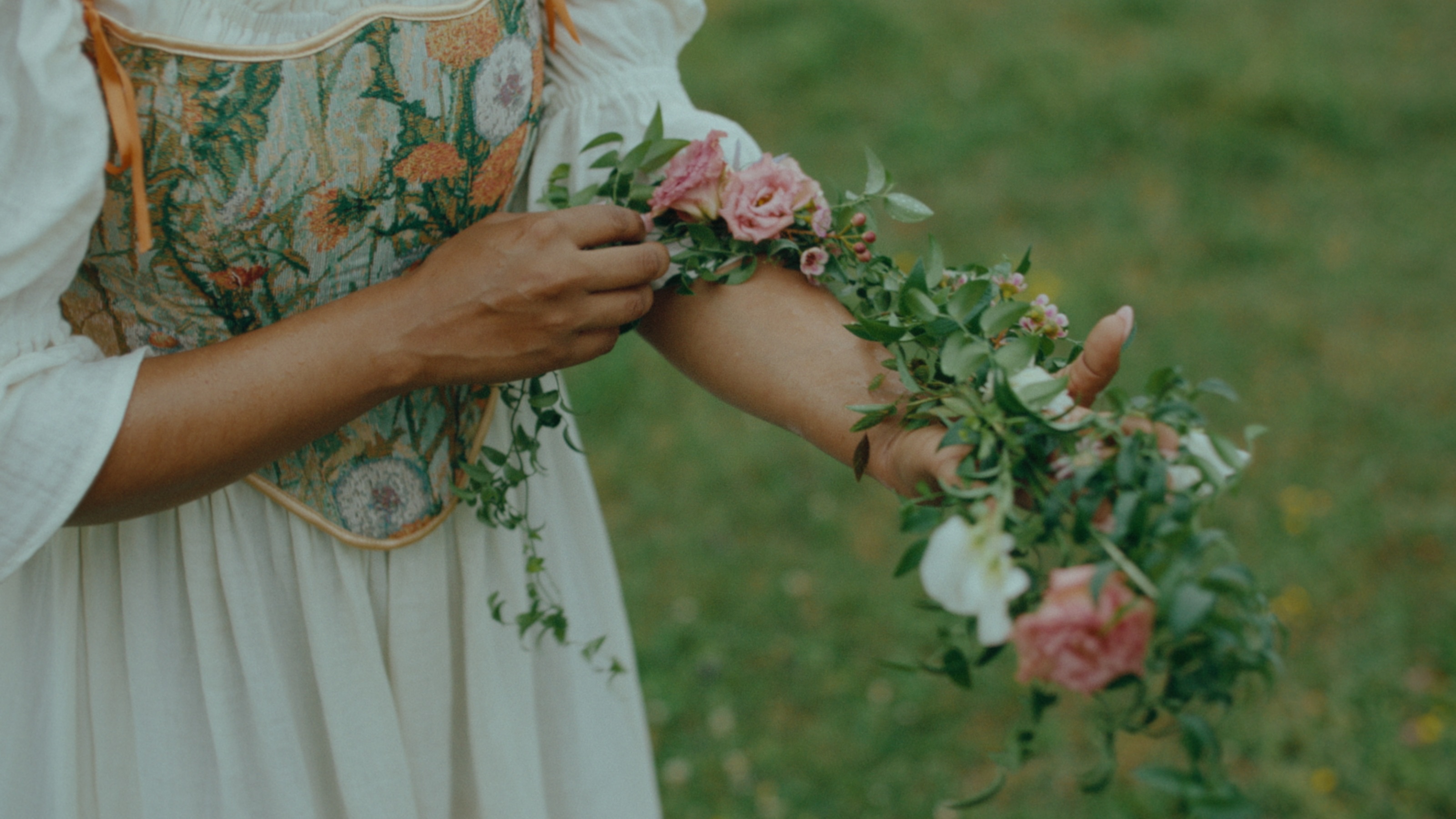 Hands weaving roses and greenery into a summer garland
