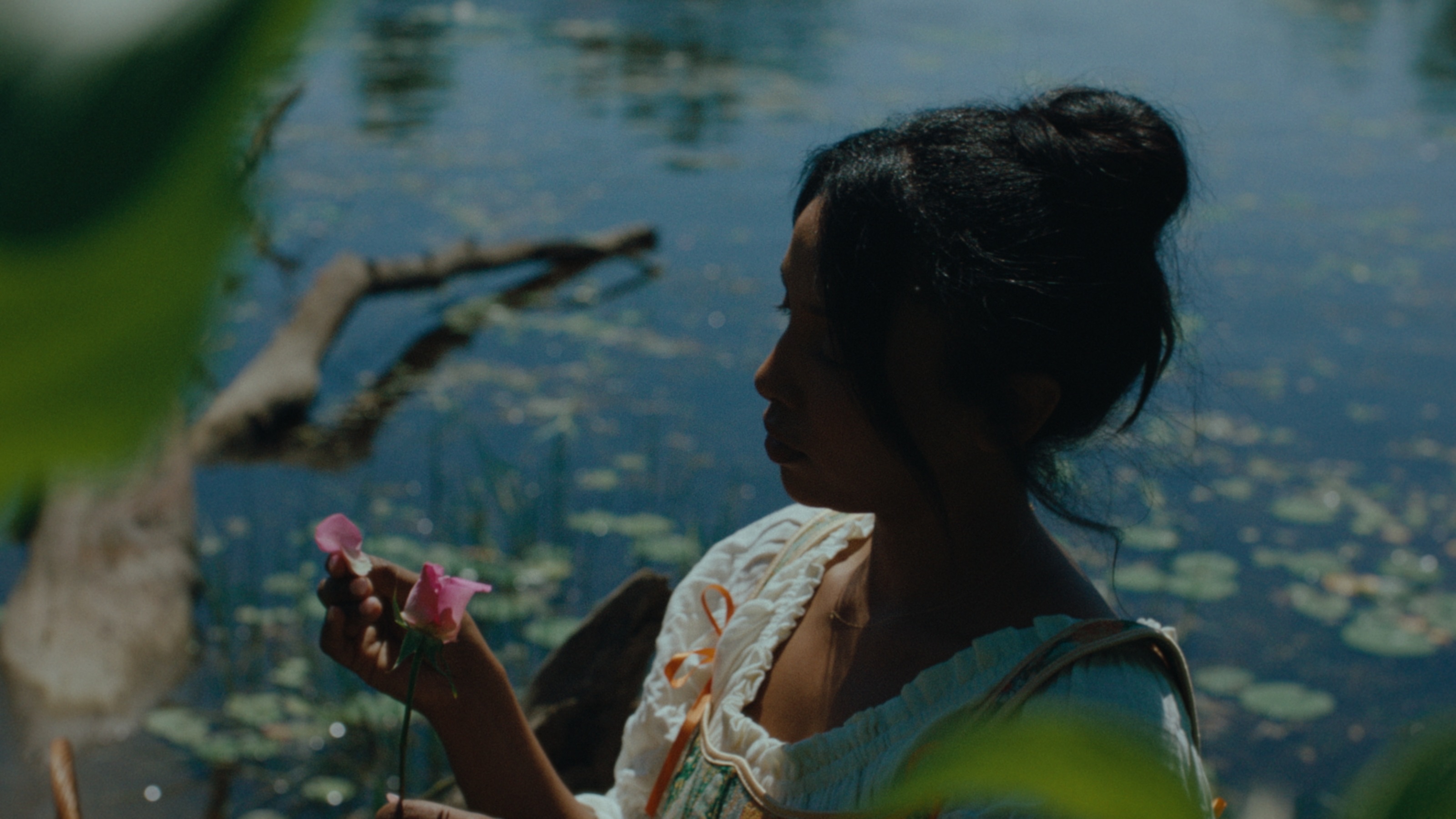 Sara holding pink roses beside a lily-covered lake