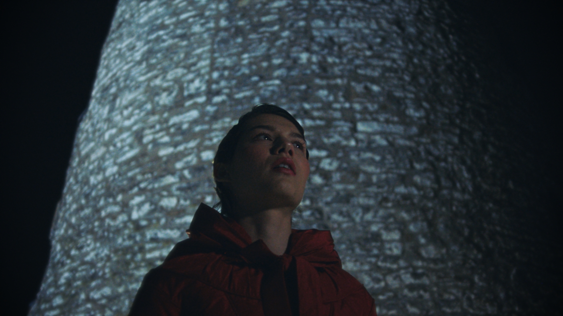 A woman in a red coat framed against the stone lighthouse