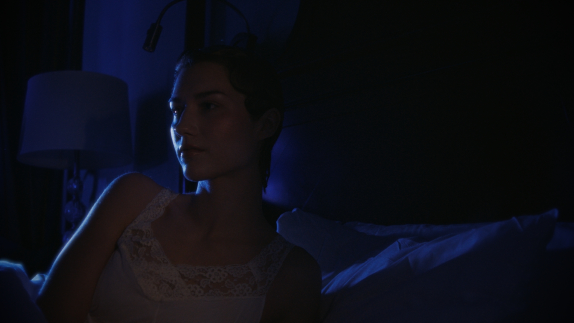 A woman waking in a bedroom washed with blue light