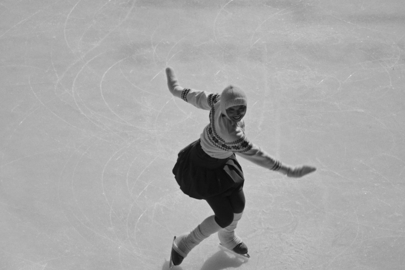 A figure skater turning across the ice in the monochrome film Gladys