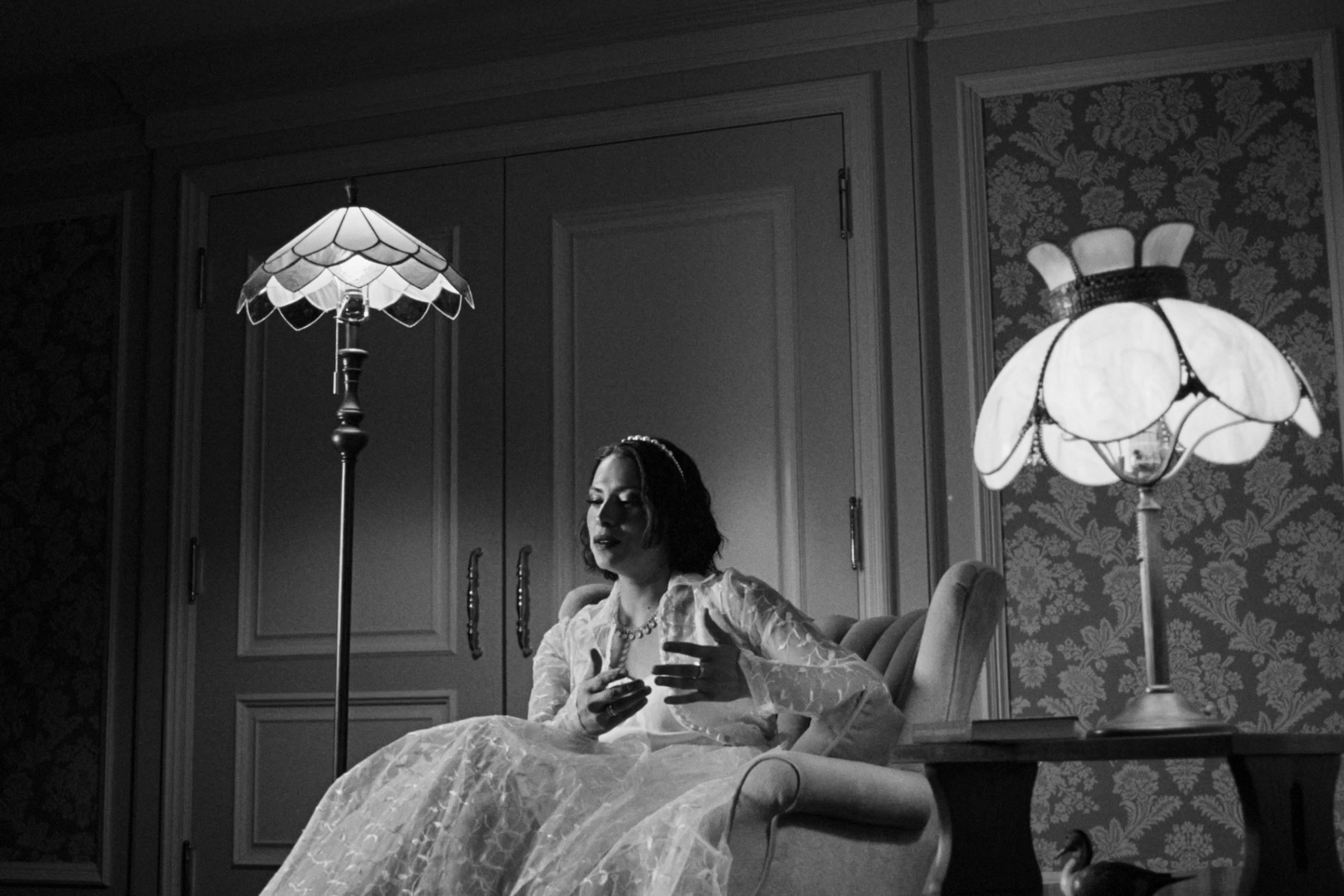Gladys seated between glowing lamps in an elegant hotel room